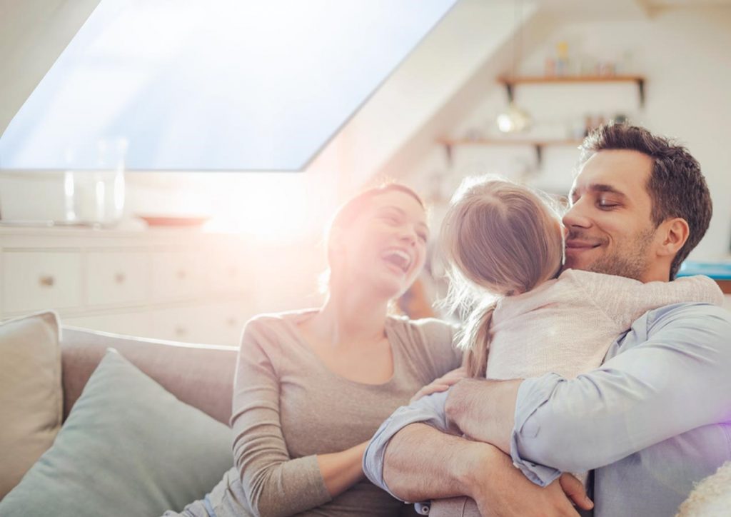 A couple and their child on a sofa with bright natural light coming from a pitched rooflight.