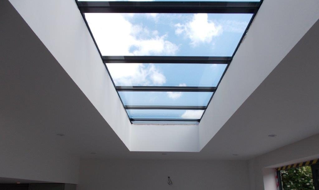 Looking up through long modular rooflight at blue sky and clouds